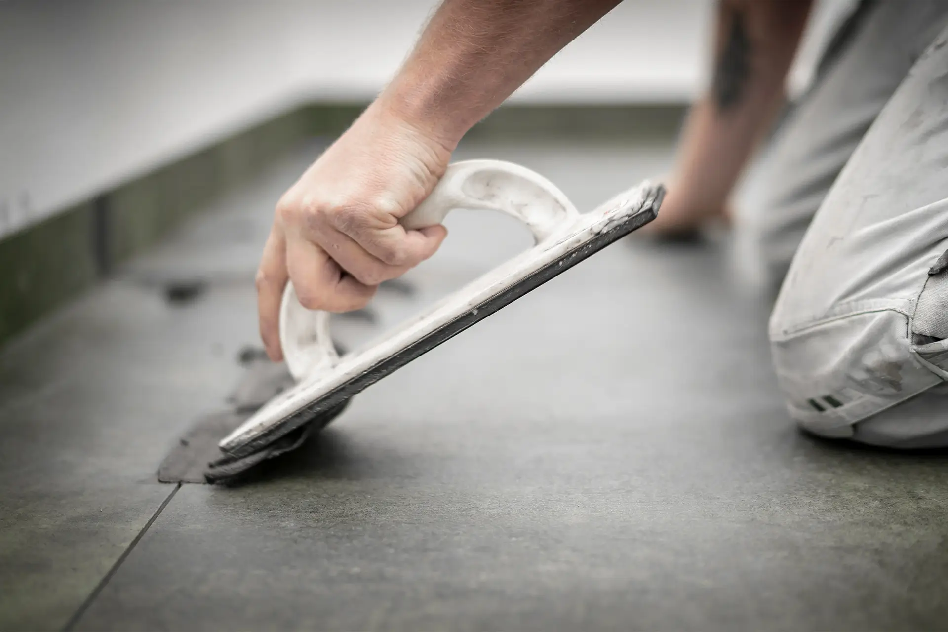 Handwerker verlegt Fliesenboden und zieht Fugenmasse mit einem Gummiwischer ab – präzise Arbeit auf einer dunklen Feinsteinzeugfläche.