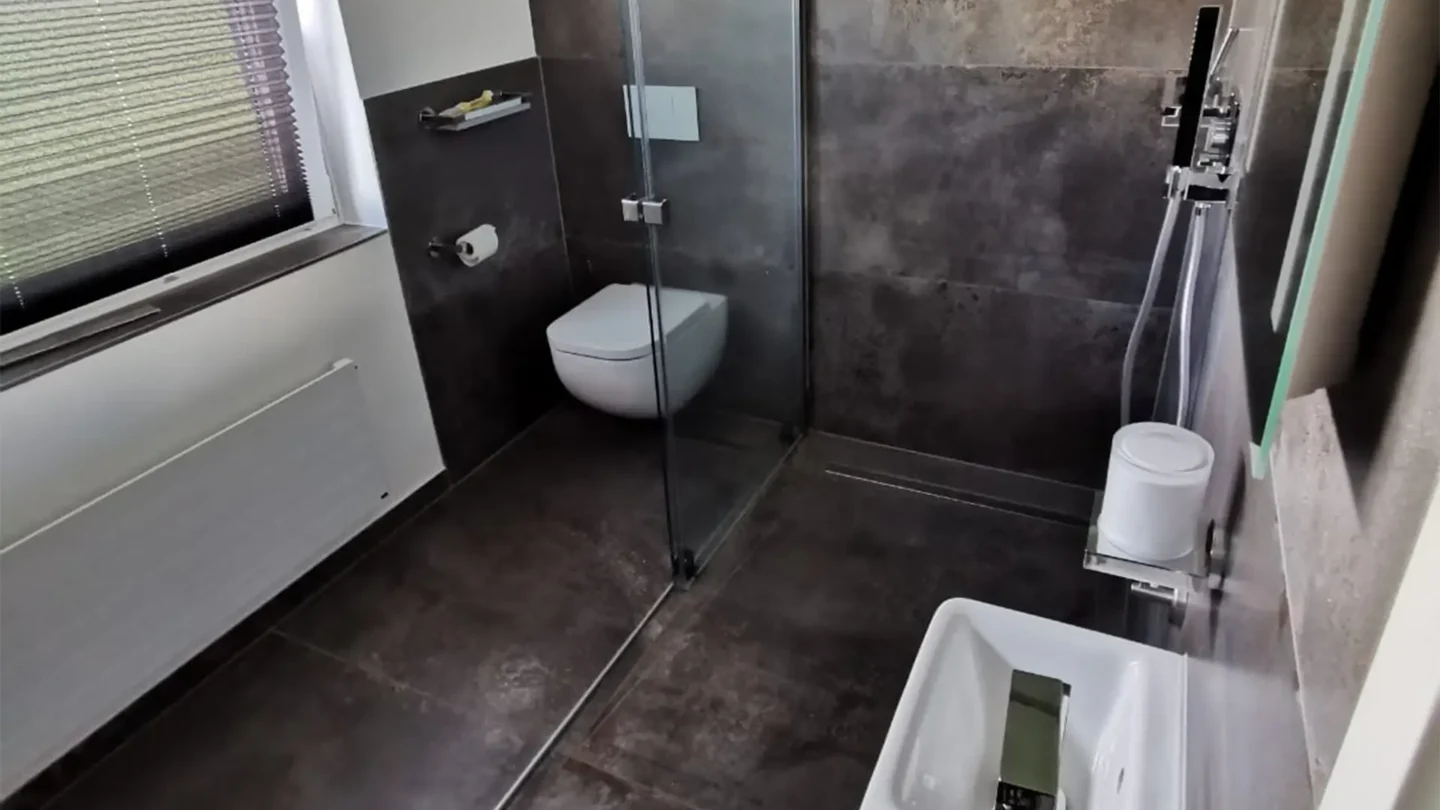 Modernes Badezimmer mit bodengleicher Dusche und großformatigen grauen Fliesen.